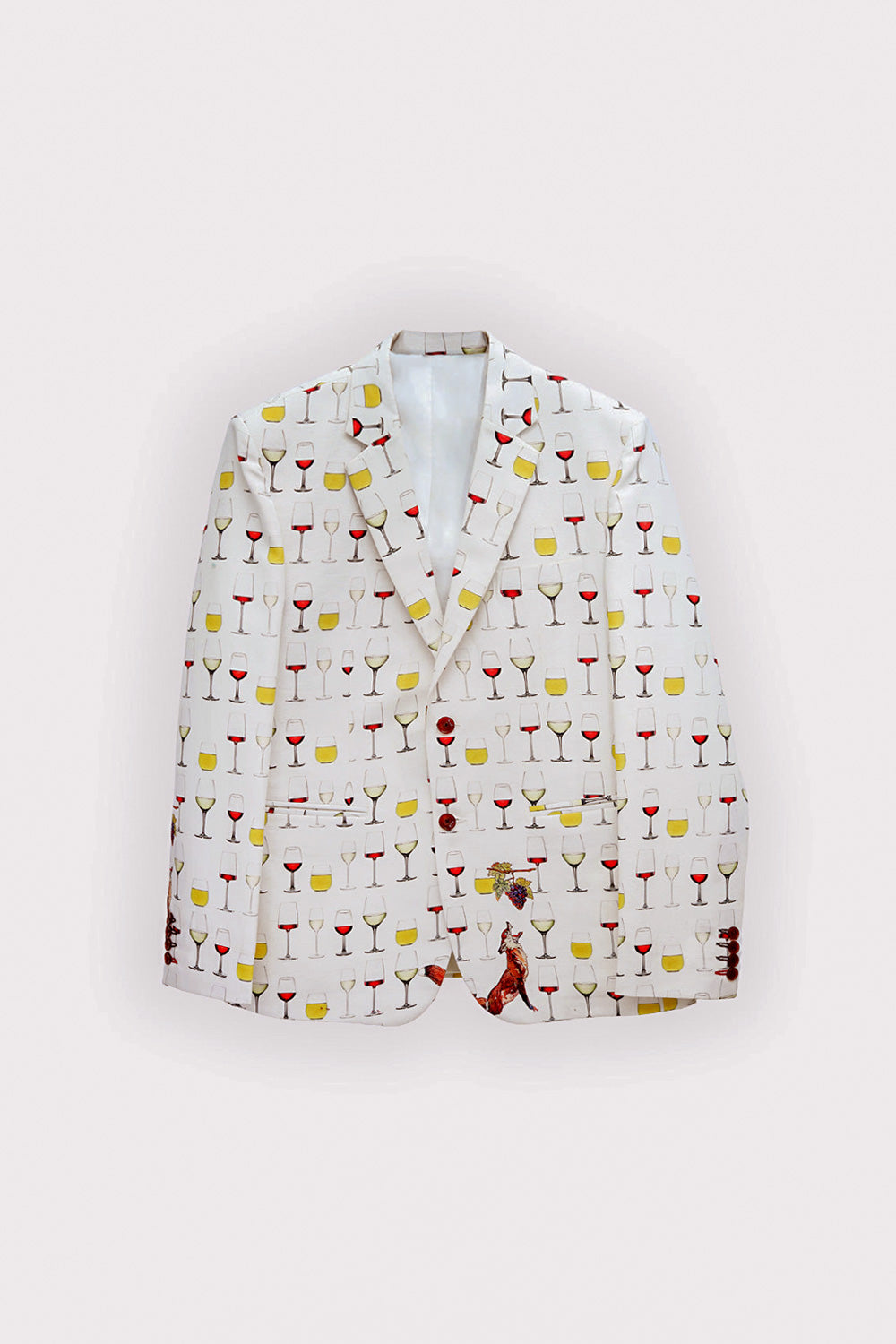 A man modeling a cream-colored blazer with a colorful cocktail glass pattern, paired with a cream turtleneck, cream trousers, and tan suede loafers, against a light gray studio background.