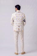 A man viewed from the back wearing a cream-colored Nehru jacket with a colorful cocktail glass pattern and beige trousers, standing against a light gray studio background.