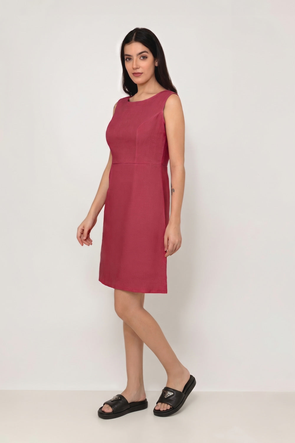 A woman modeling a sleeveless, knee-length dusty rose pink linen dress with structured shoulders, standing against a plain white studio background.