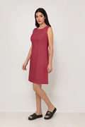 A woman modeling a sleeveless, knee-length dusty rose pink linen dress with structured shoulders, standing against a plain white studio background.