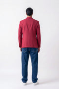 A man viewed from behind wearing a red linen blazer, blue jeans, and white sneakers against a plain white studio background.