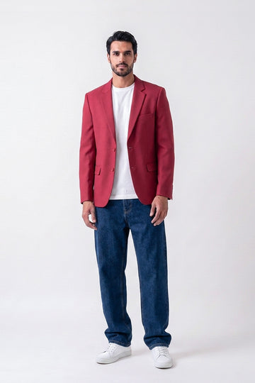 A man modeling a red linen blazer over a white t-shirt, blue jeans, and white sneakers, standing against a plain white studio background.