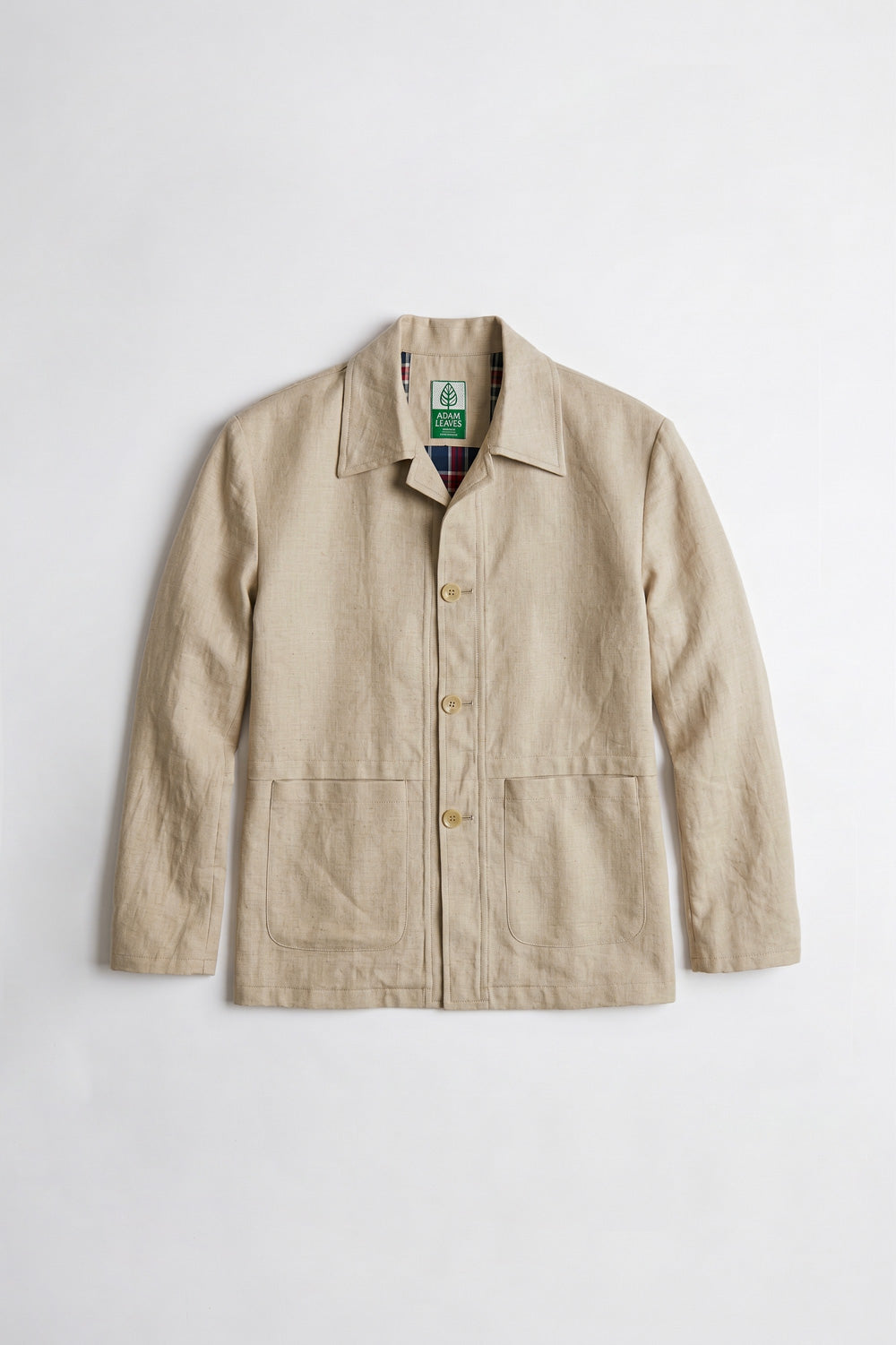 A man stands against a light gray studio background wearing a beige utility linen jacket over a white T-shirt, olive green cargo pants, and black shoes.