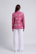 A model shown from the back wearing a pink floral silk blazer and white wide-leg trousers against a light gray studio background.