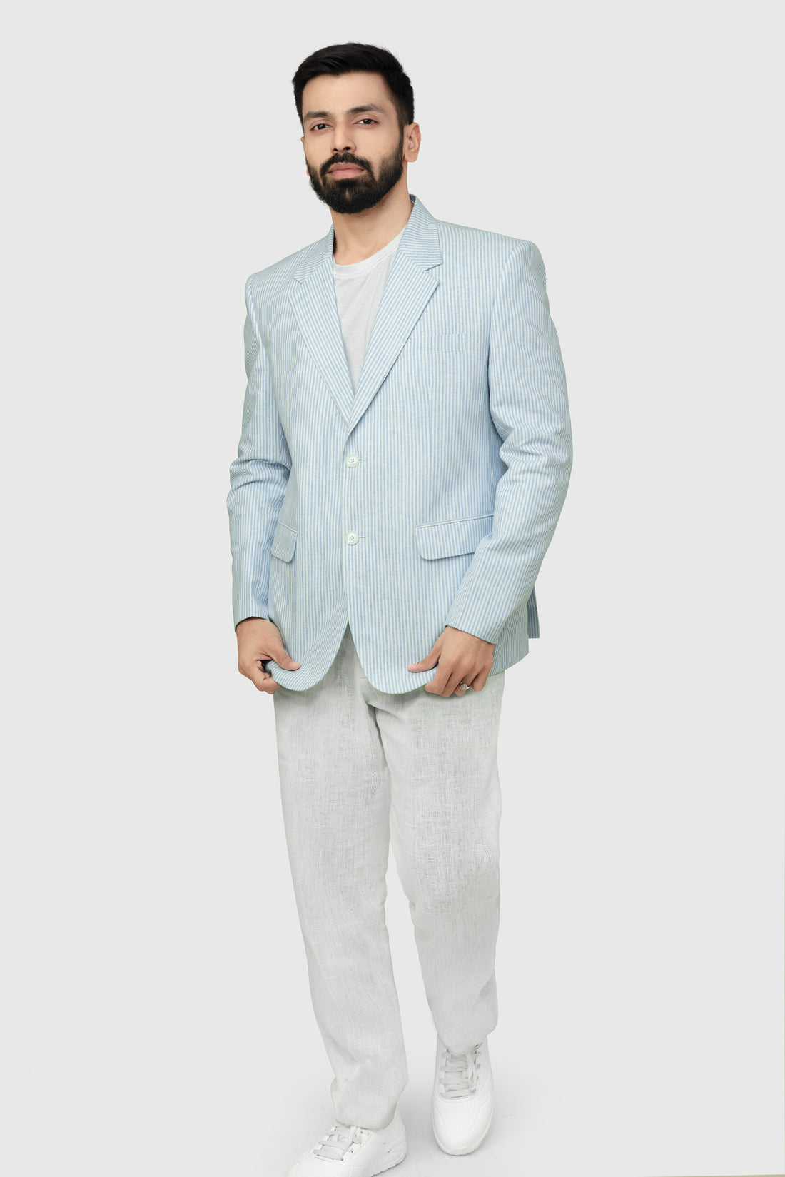 A male model wearing a light blue linen blazer with a Notch Lapel, two buttons, and two patch pockets on the front, paired with light-colored trousers.