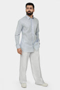 A man standing, wearing a linen shirt with a cut-away collar, long sleeves, and a single-button cuff, paired with light-colored trousers.