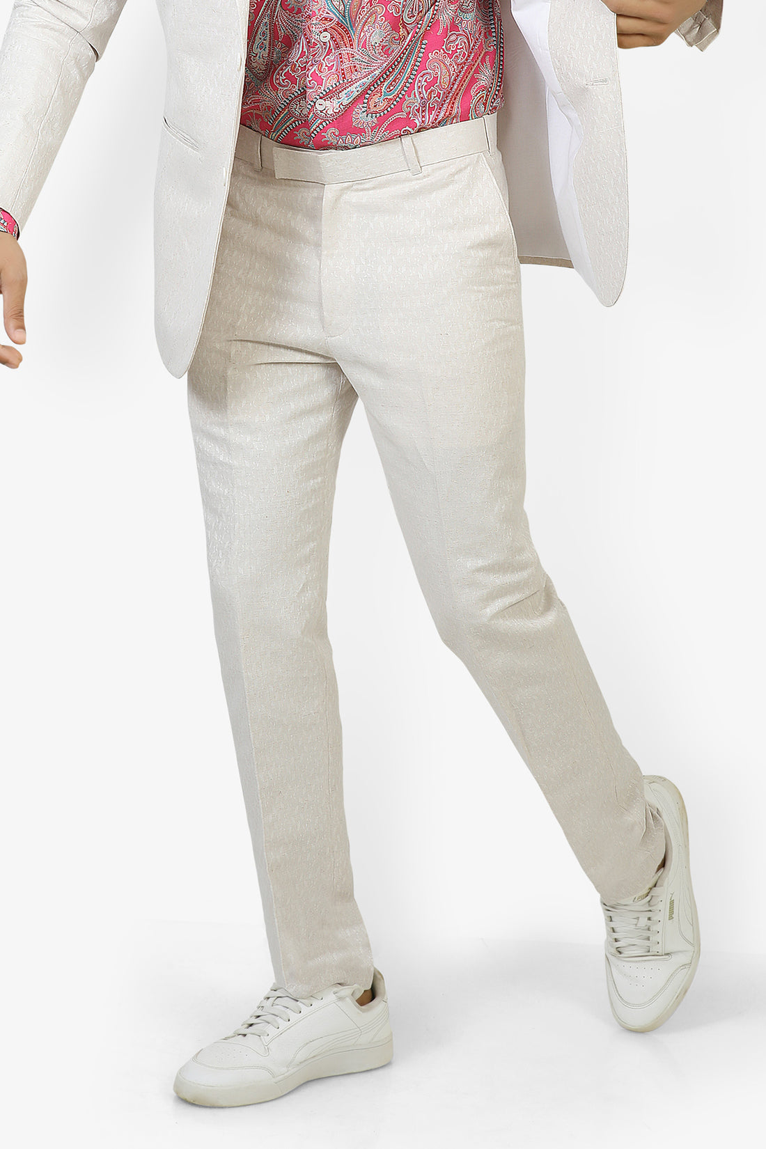 A man wearing white linen trousers with a white jacket and a multicolored shirt, standing against a white background.