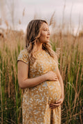 Pregnant woman wearing a mustard yellow botanical eco-printed maternity dress in a natural field, sustainable maternity fashion