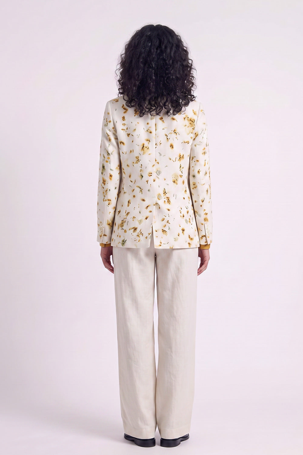 A model shown from the back wearing a cream-colored hemp blazer with a gold floral eco-print and matching cream trousers, set against a plain light background.