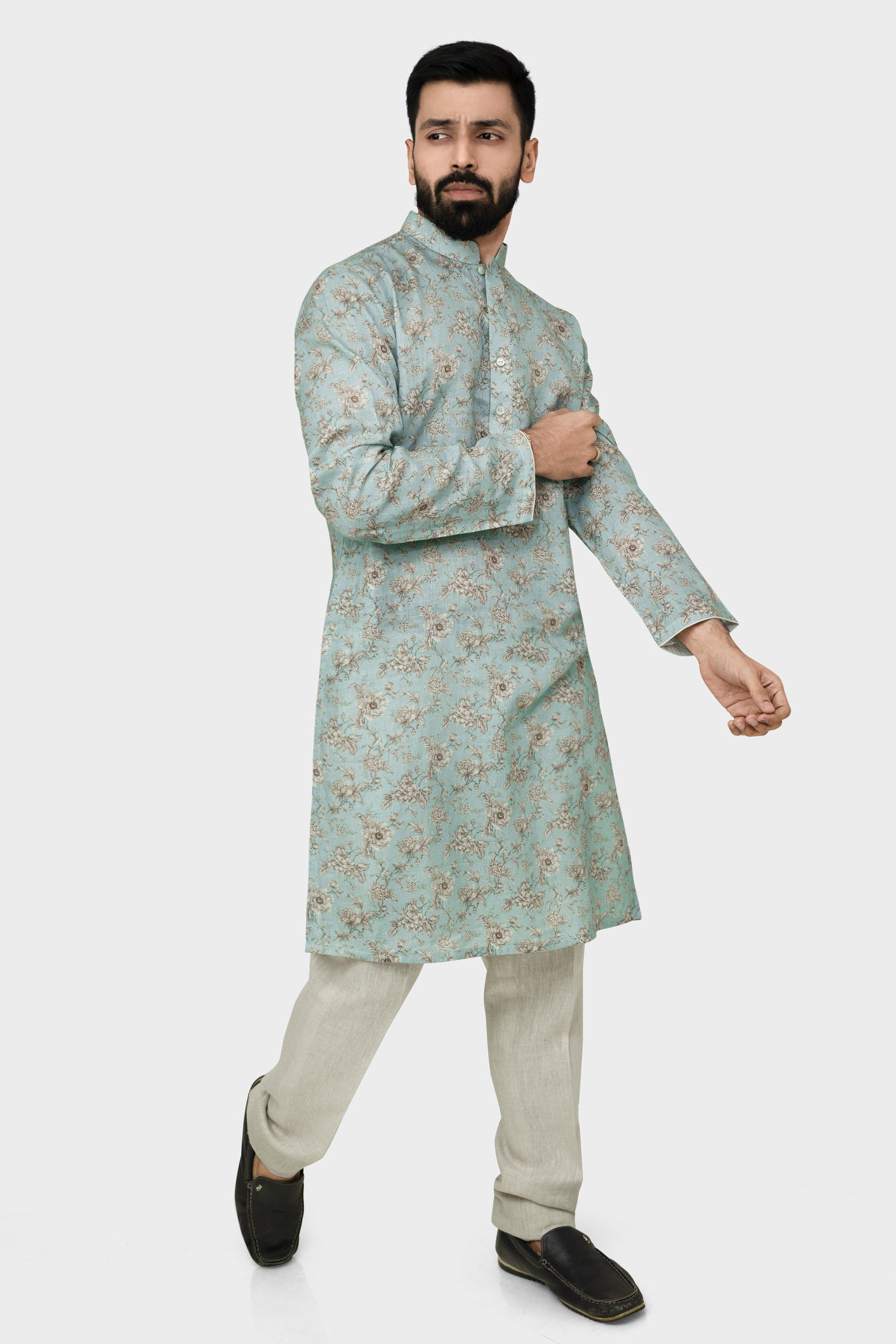 A man wearing a traditional Indian linen kurta with a mandarin collar, featuring a floral print and matching buttons, paired with light-colored trousers.