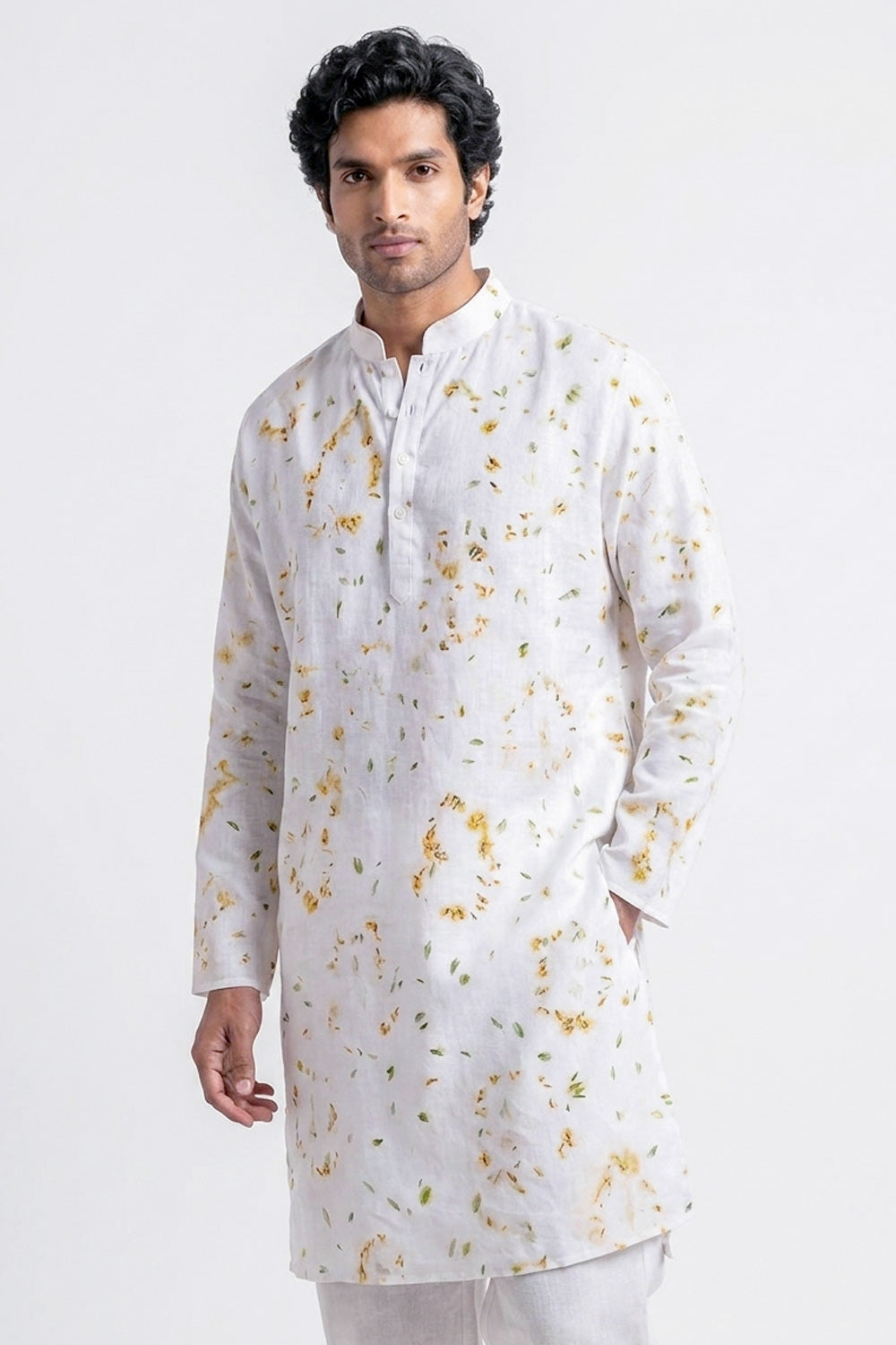 A man wearing a white long-sleeve kurta with a delicate yellow and green floral print, photographed against a plain light gray studio background.