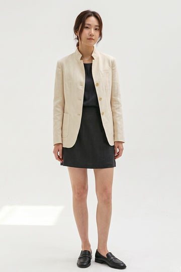 Model wearing the Assam Muga silk jacket in natural gold with a black top, mini skirt and loafers