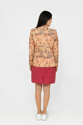 A woman shown from the back wearing a patterned beige and orange long-sleeve linen blazer with a dark red skirt and white sneakers, standing against a plain white studio background.