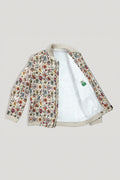 A bomber linen jacket with a dense multicolor floral print on a cream base, featuring a white sherpa lining and ribbed beige trim, shown open against a light gray background.
