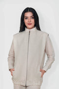 A woman modeling a light beige sleeveless zip-up linen vest with a high stand-up collar and front pockets, set against a plain light gray studio background.