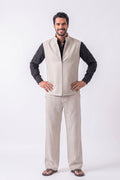 A man modeling a light beige linen vest and matching trousers over a black long-sleeve shirt, standing against a plain white studio background.