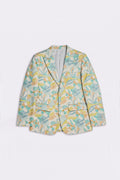 A women's single-breasted silk blazer with a tropical leaf pattern in shades of teal, yellow, and green on a light cream background, displayed flat against a light gray background.