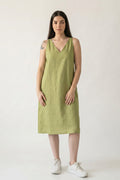 A woman modeling a sleeveless olive green hemp midi dress with a V-neckline, paired with white sneakers, against a plain off-white studio background.