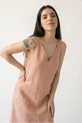 A woman modeling a sleeveless dusty pink hemp dress with a V-neckline, photographed against a plain off-white background.