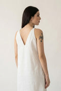 A woman shown from the back wearing a white sleevelesshemp dress with a deep V-neckline, set against a plain off-white studio background.