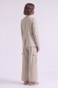 A model shown from the back wearing a light beige textured linen jacket and matching wide-leg cargo pants against a plain light gray studio background.