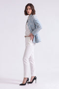 A woman modeling a light blue embroidered linen blazer, white top and trousers, and black heels against a plain white studio background.