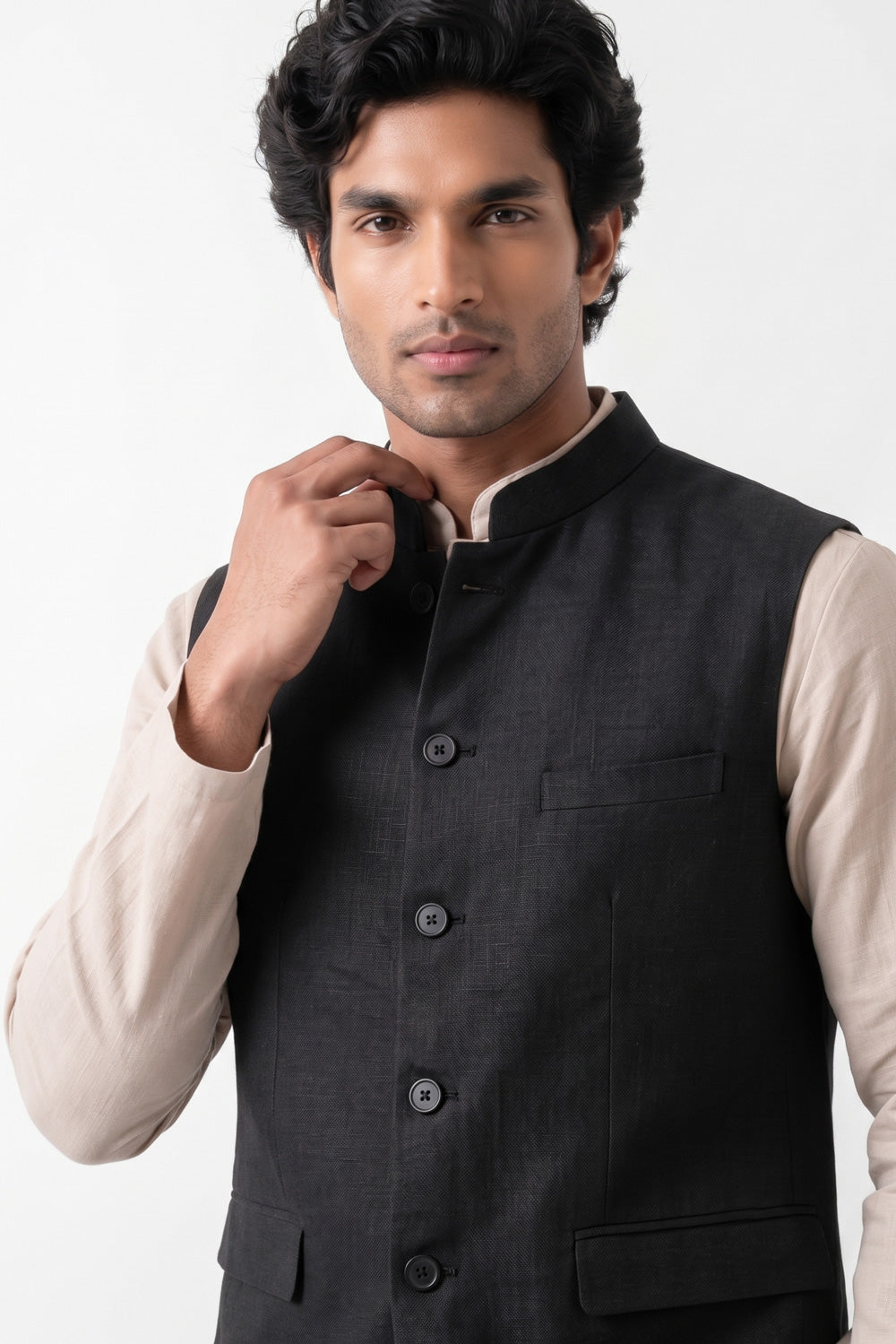 A man wearing a dark charcoal gray linen vest over a light beige long-sleeve shirt, posing against a plain white studio background.