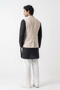 A man wearing a beige tailored linen waistcoat over a pale blue long-sleeve kurta, standing against a neutral studio background.