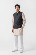 A man modeling a traditional Indian outfit consisting of a black button-up linen waistcoat (kurta) layered over a beige long-sleeve shirt, paired with white trousers and white shoes, against a plain light gray background.