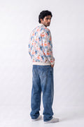 A man wearing a colorful floral print bomber Hemp jacket, blue jeans, and white sneakers, standing in profile against a plain white studio background.