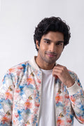 A man wearing a white crewneck t-shirt and a colorful bomber hemp jacket with a watercolor floral pattern in blue, orange, and pink, posed against a light gray background.