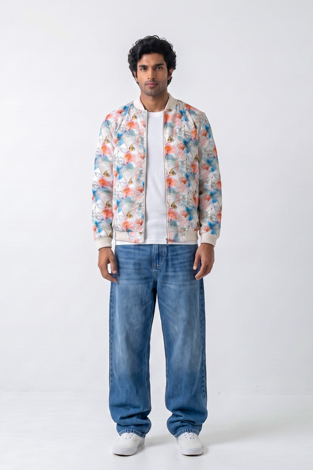 A man modeling a white bomber hemp jacket with a colorful floral print, worn over a white t-shirt and blue jeans, against a plain white studio background.