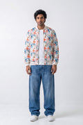 A man modeling a white bomber hemp jacket with a colorful floral print, worn over a white t-shirt and blue jeans, against a plain white studio background.