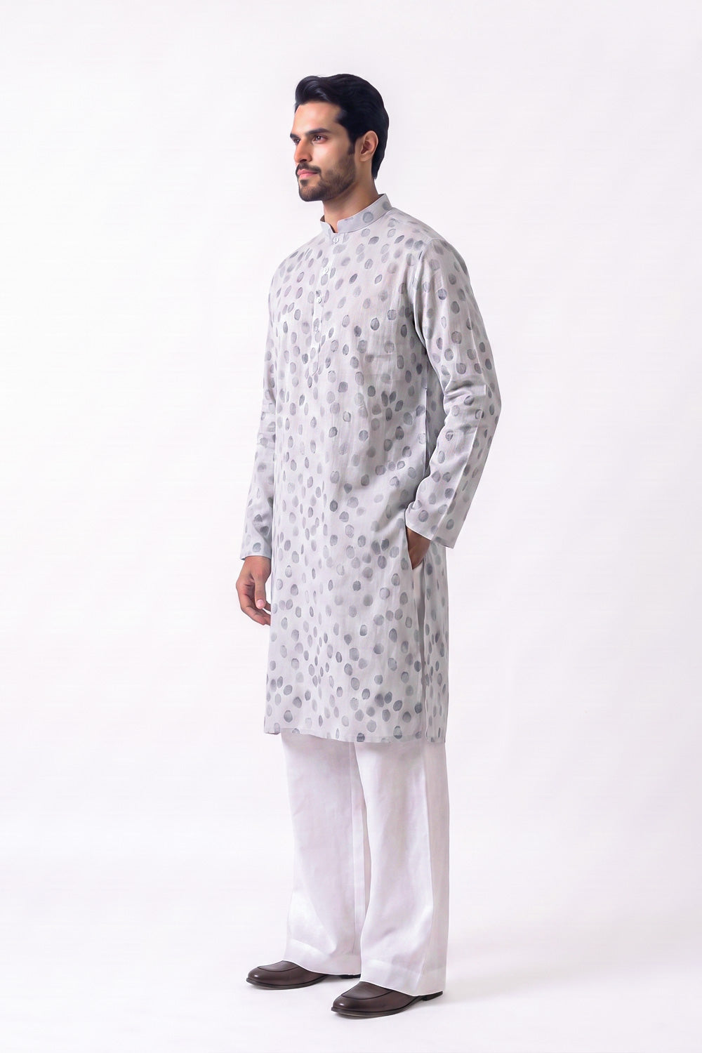 A man modeling a light gray long-sleeve hemp kurta with a subtle circular pattern, paired with white trousers and dark brown shoes, standing against a plain white studio background.