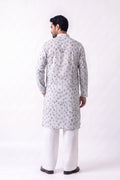 A man viewed from the back wearing a light gray long hemp kurta with a repeating circular pattern, paired with white trousers and dark brown shoes, against a plain white studio background.
