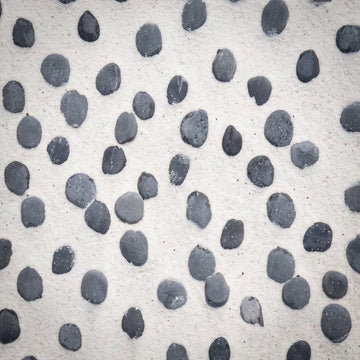 A close-up of a textured white surface covered with small, irregular dark gray to black pebble-like spots.