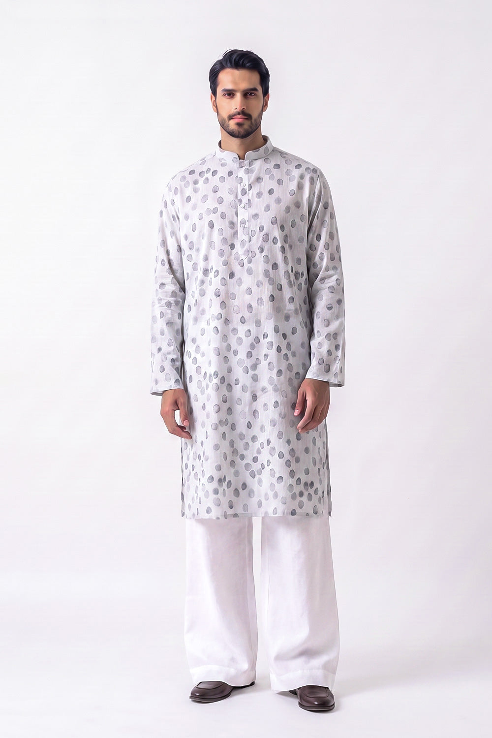 A man modeling a light gray long-sleeve hemp kurta with a silver-gray circular pattern, paired with white trousers and dark brown shoes, standing against a plain white studio background.