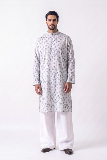 A man modeling a light gray long-sleeve hemp kurta with a silver-gray circular pattern, paired with white trousers and dark brown shoes, standing against a plain white studio background.