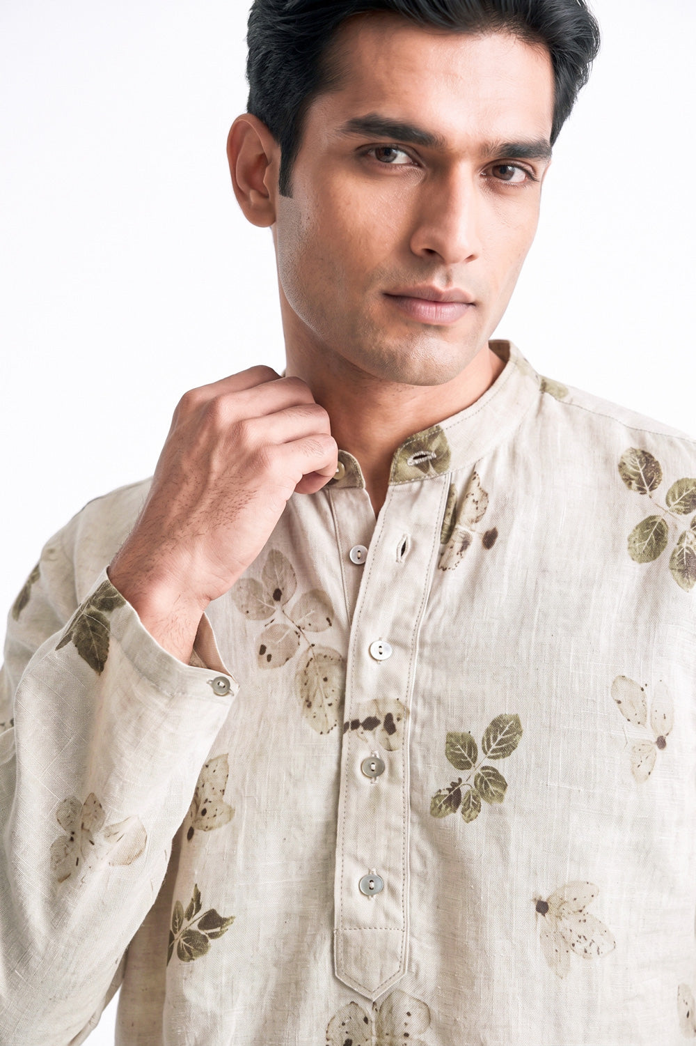A man wearing a light beige linen kurta with a green and brown leaf pattern, shown in a close-up portrait against a white background.