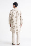 A man viewed from the back wearing a light beige kurta and matching trousers, both decorated with a subtle brown floral pattern, set against a plain white studio background.