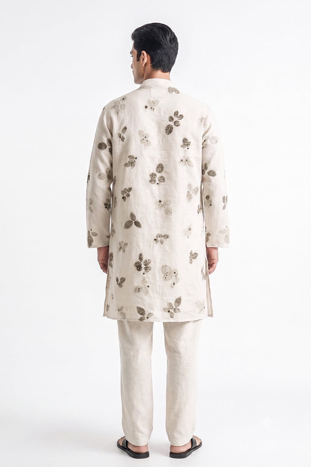 A man viewed from the back wearing a light beige kurta and matching trousers, both decorated with a subtle brown floral pattern, set against a plain white studio background.