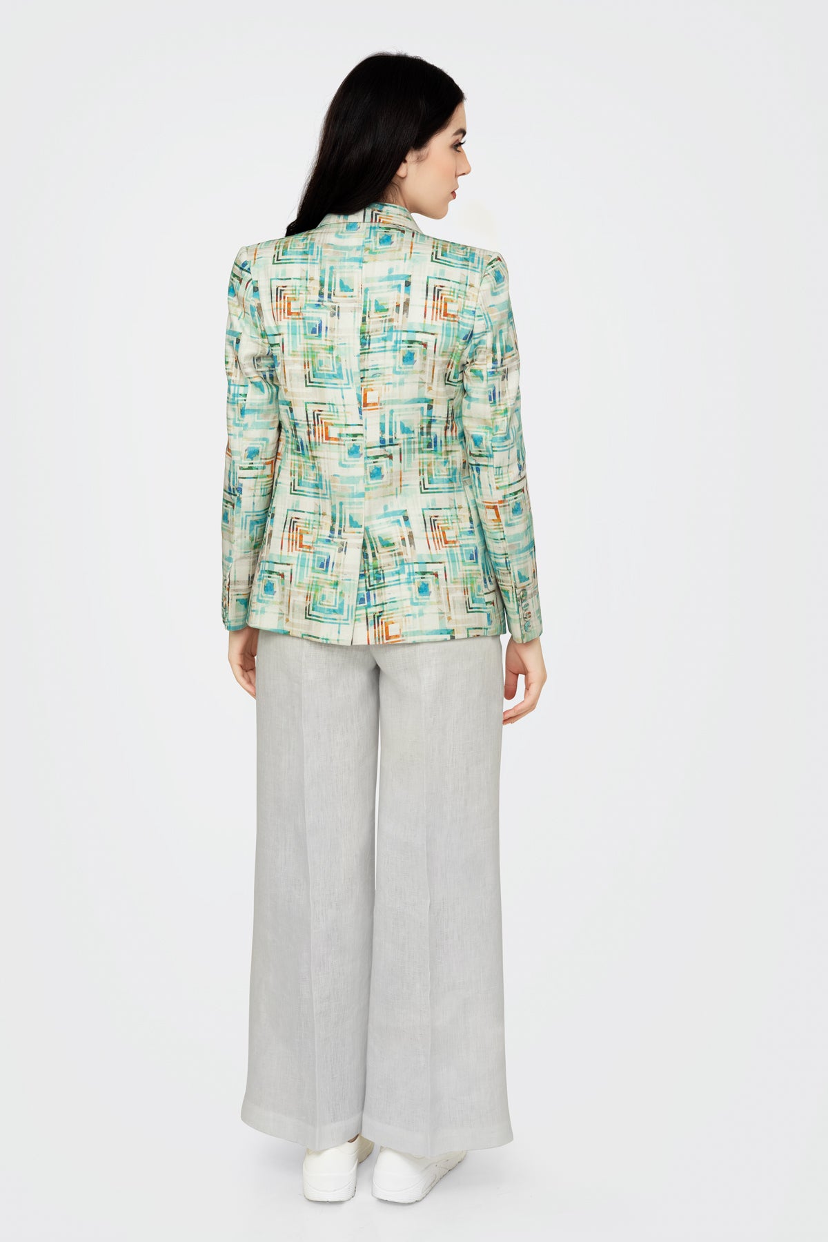 Woman wearing a patterned jacket and light gray pants on a white background
