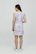 A woman standing in a studio setting, wearing a mid-length floral hemp seersucker dress with a boat neckline and sleeveless top, paired with white sneakers.