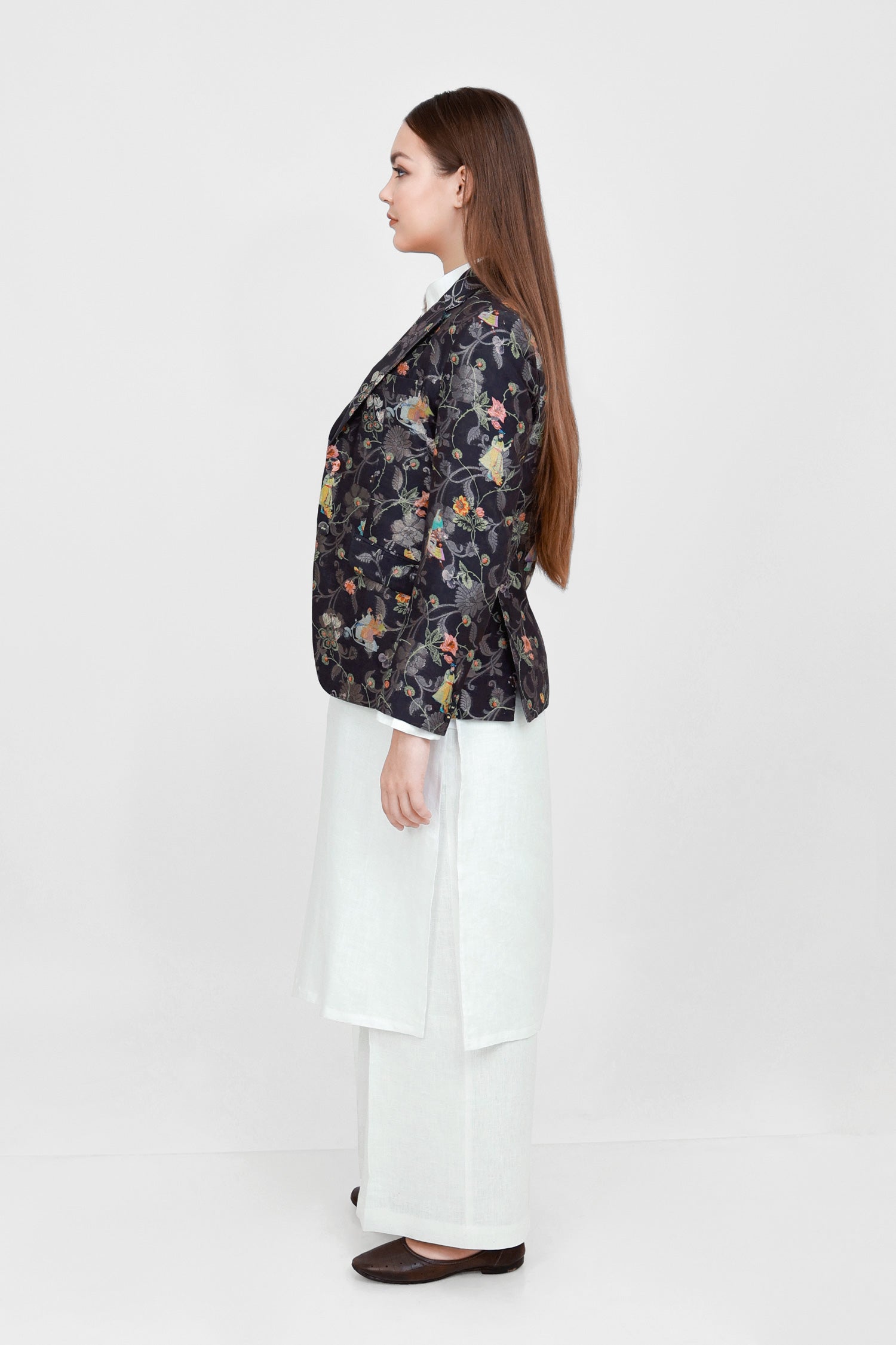 A woman modeling a silk blazer with a floral pattern, wearing a white shirt and pants.