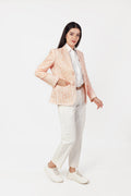 Woman wearing a peach blazer over a white shirt and pants on a white background