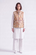 A model wearing a white traditional outfit consisting of a long-sleeve kurta, wide-leg trousers, and white sneakers, layered with a sleeveless  linen  vest featuring a detailed multicolor illustration pattern.