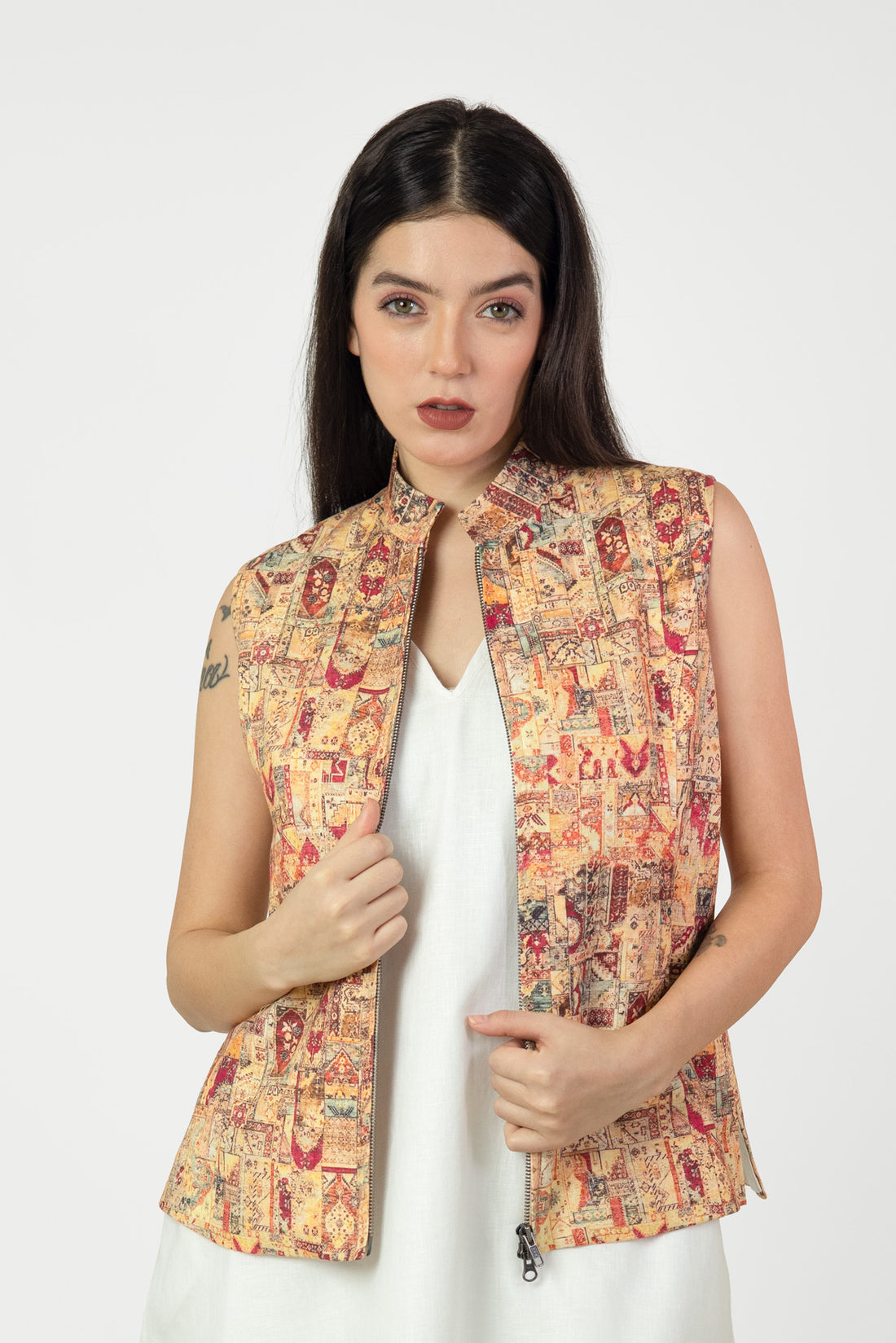 Woman wearing a patterned vest over a white dress on a white background