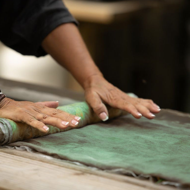 A close-up of a person's hands rolling out a green fabric or mat on a wooden surface.