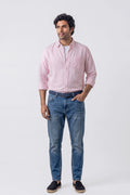 A man modeling a light pink long-sleeve button-down linen shirt and blue jeans against a plain light gray studio background.