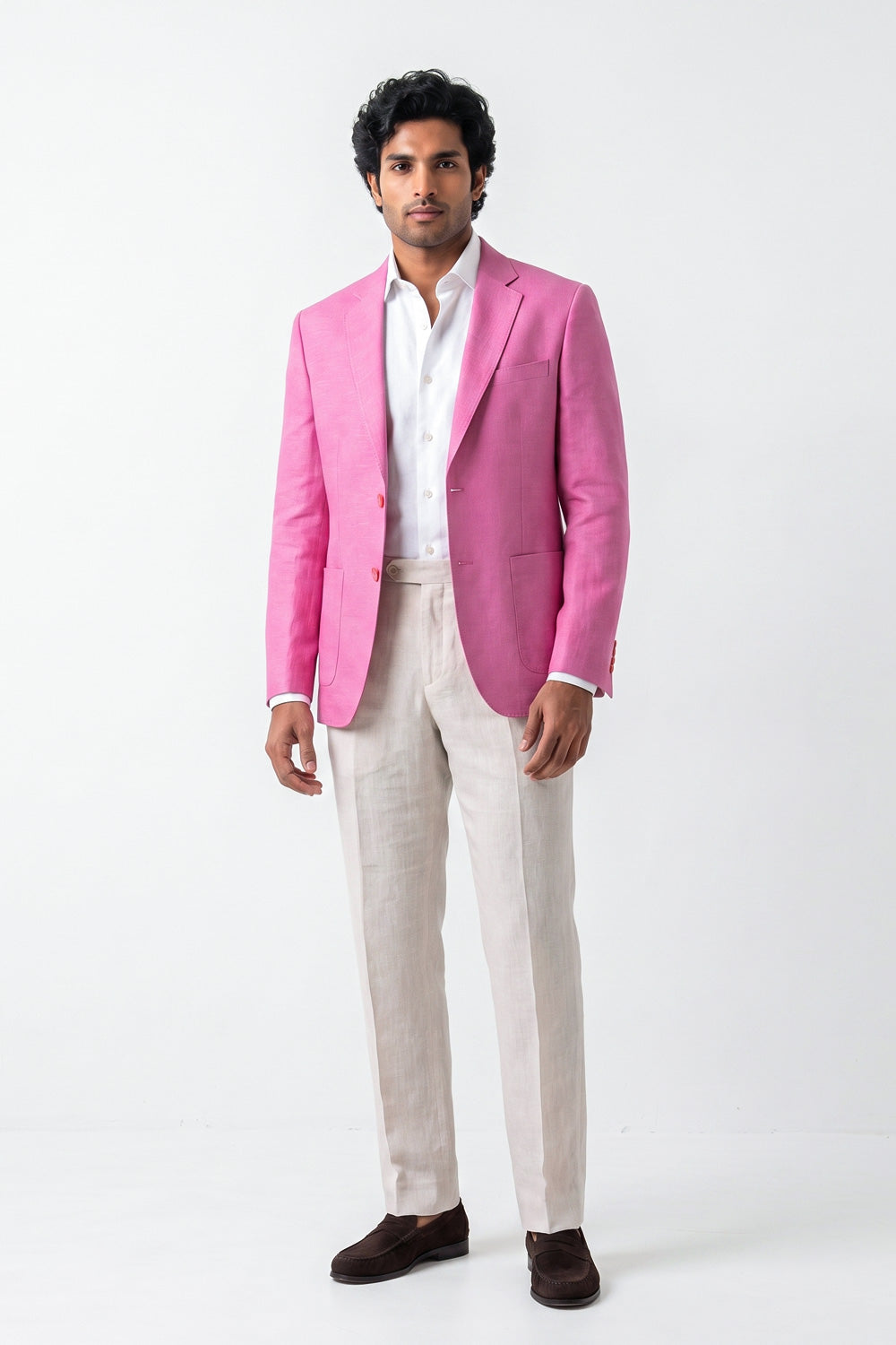 A man modeling a bright pink hemp blazer over a white dress shirt, paired with light beige trousers and dark brown loafers, standing against a plain white studio background.